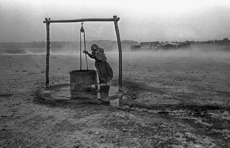 A woman is drawing water from a well during a strong sandstorm known as an “Afghan storm.” Northern Afghanistan, October, 2001. Photo by Oleg Klimov